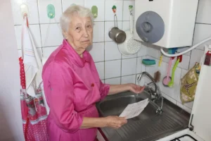 Пенсионерка возле крана с водой